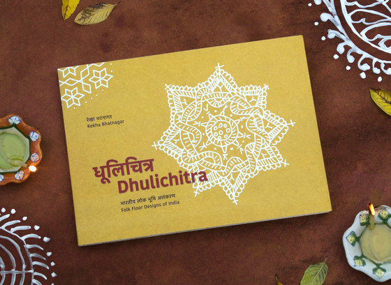 Photograph of Dhulichitra book with floor decorations, earthen lamps and fallen leaves around