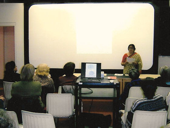 Photograph of Rekha giving a talk to an audience in an art gallery